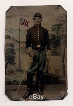 STRIKING CIVIL WAR TINTYPE OF UNION SOLDIER WITH COLOR BACKDROP FLAG SWORD