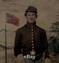 STRIKING CIVIL WAR TINTYPE OF UNION SOLDIER WITH COLOR BACKDROP FLAG SWORD